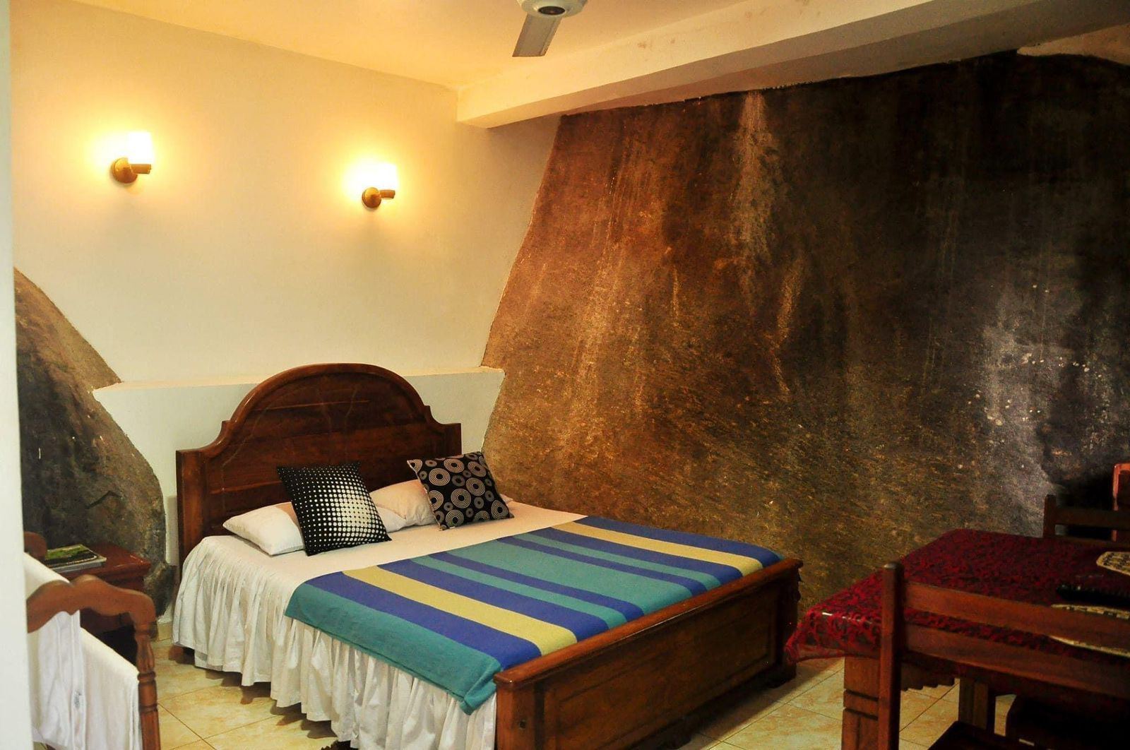 Bedroom with a natural granite boulder forming one wall, lit by warm wall lamps